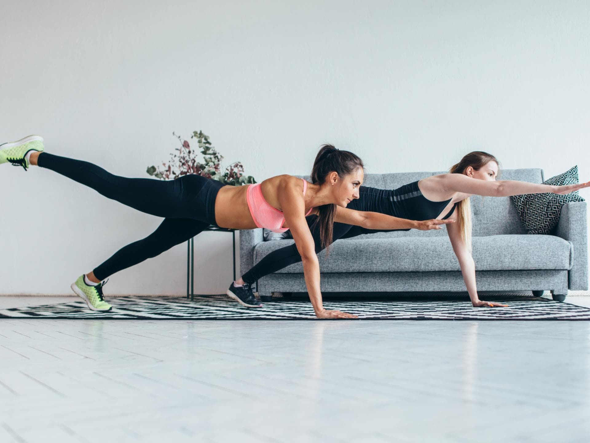 Frauen machen Planks mit Arm- und Beinheber in Wohnzimmer
