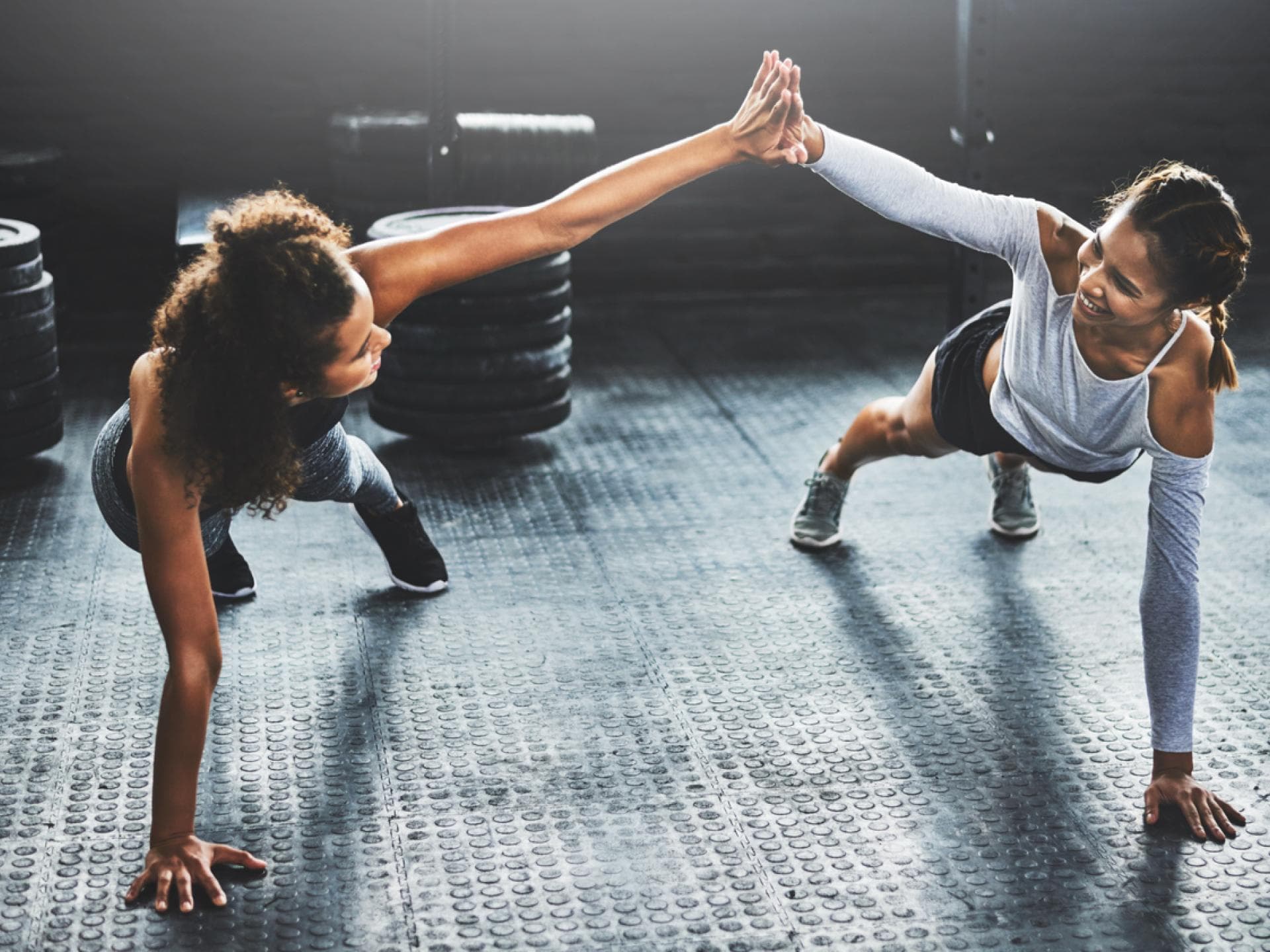 Die Partner-Plank spornt an und macht Spaß zwei Fitnessfreundinnen machen Plank zusammen und klatschen ab