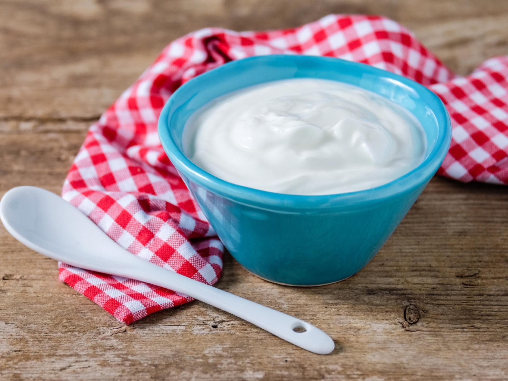 Joghurt in Schüssel auf kariertem Tuch auf Tisch