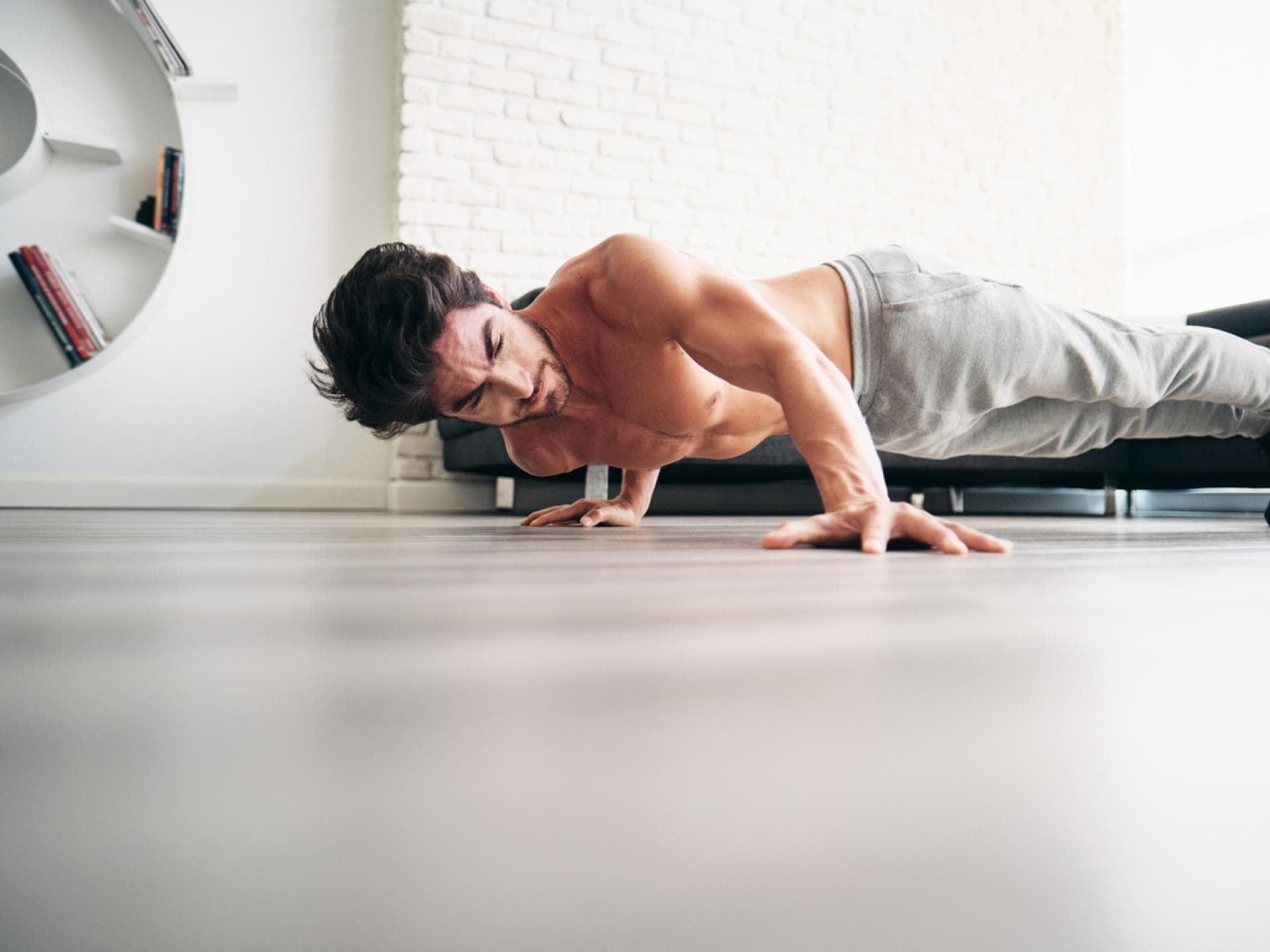 Die Variante erfordert viel Körperkontrolle Mann macht Archer Push-ups in der Wohnung