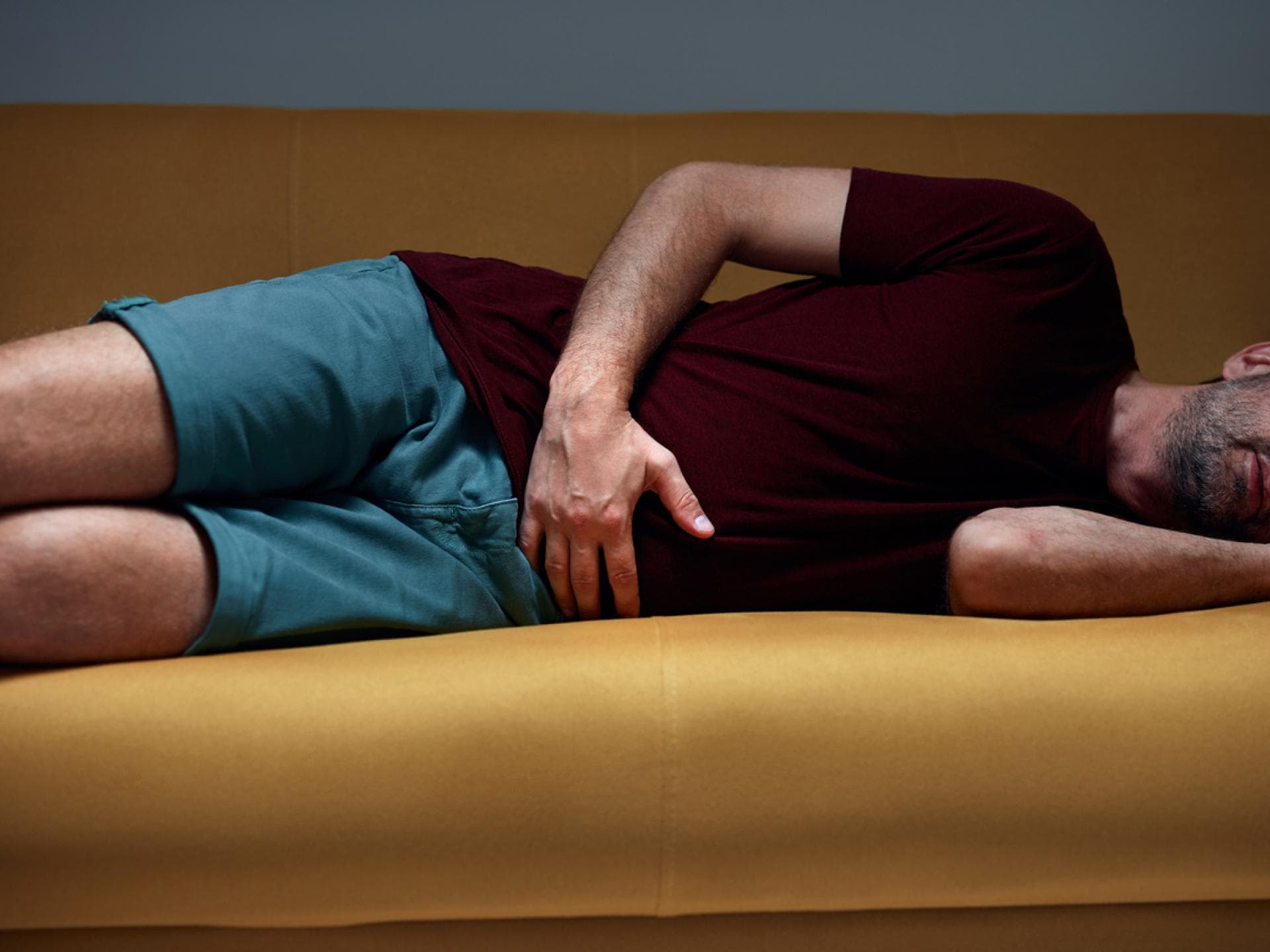 Mann mit Bauchschmerzen liegt auf gelber Couch