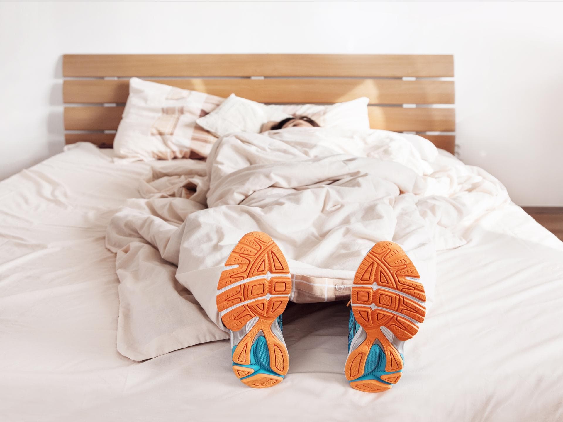 Sportler liegt mit Sportschuhen im Bett