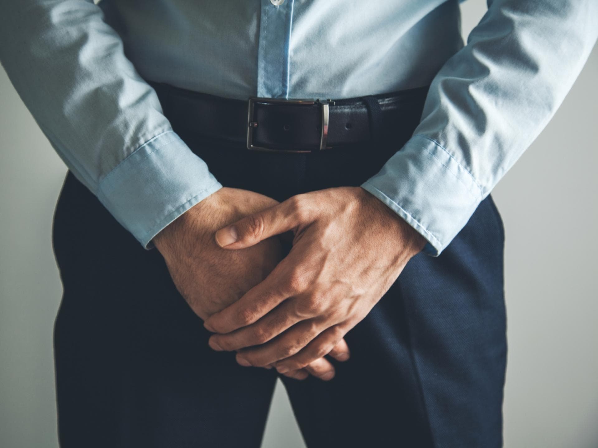 Mann verschränkt Hände vor Schritt