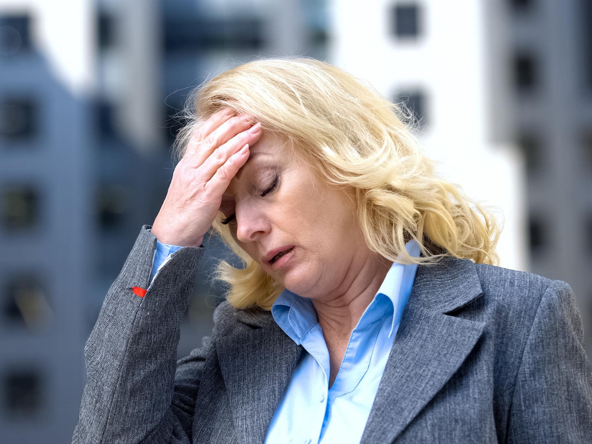 Blonde Frau mit Burnout fasst sich erschöpft an den Kopf