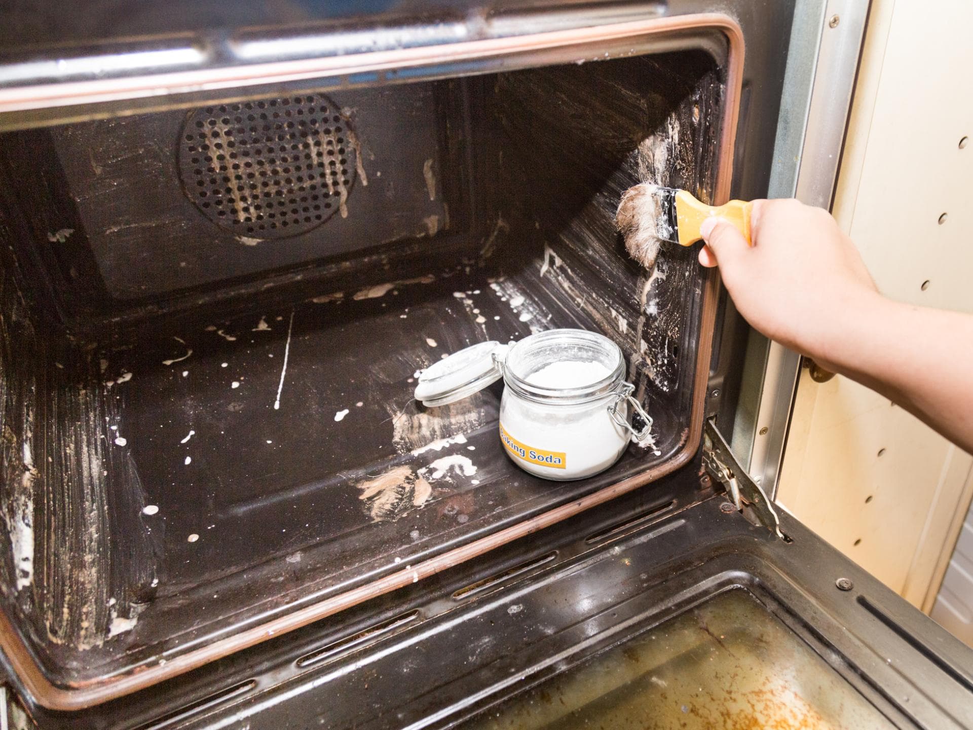 Frau reinigt Backofen mit dem Hausmittel Backpulver