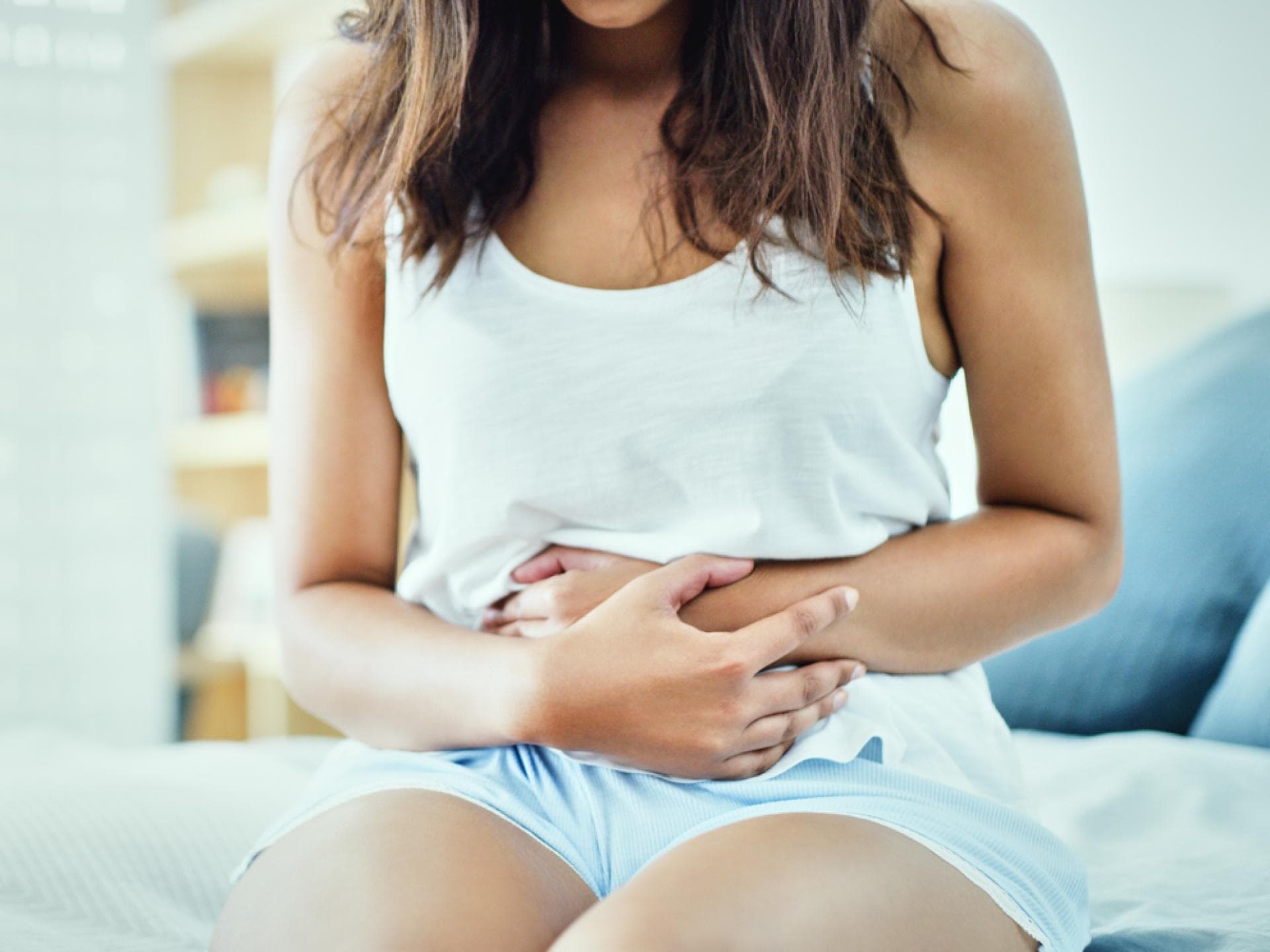 Reizdarmsymptome bei Frauen können sehr vielfältig sein Frau sitzt auf Bett und hält sich schmerzenden Bauch mit beiden Händen