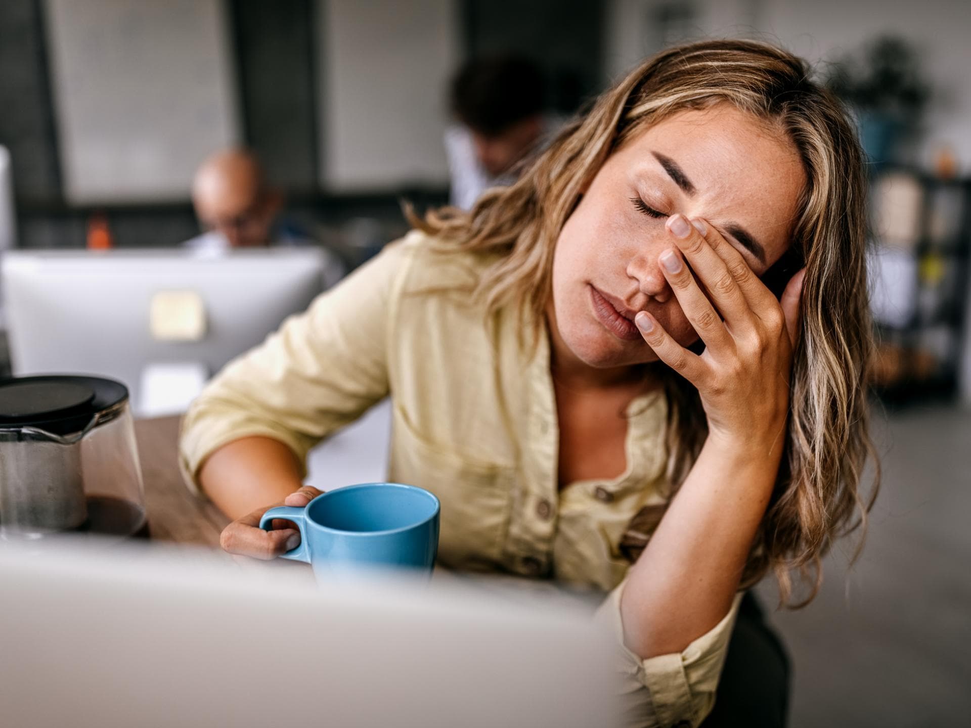 Symptome des Zuckerentzugs sind Müdigkeit und Kopfschmerzen Müde Frau sitzt mit geschlossenen Augen und Kaffeebecher vor dem Laptop