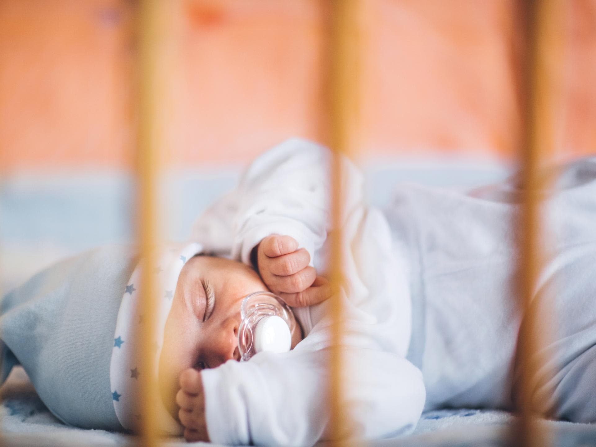 Ein Baby schläft in einem Bettchen mit einem Schnuller.