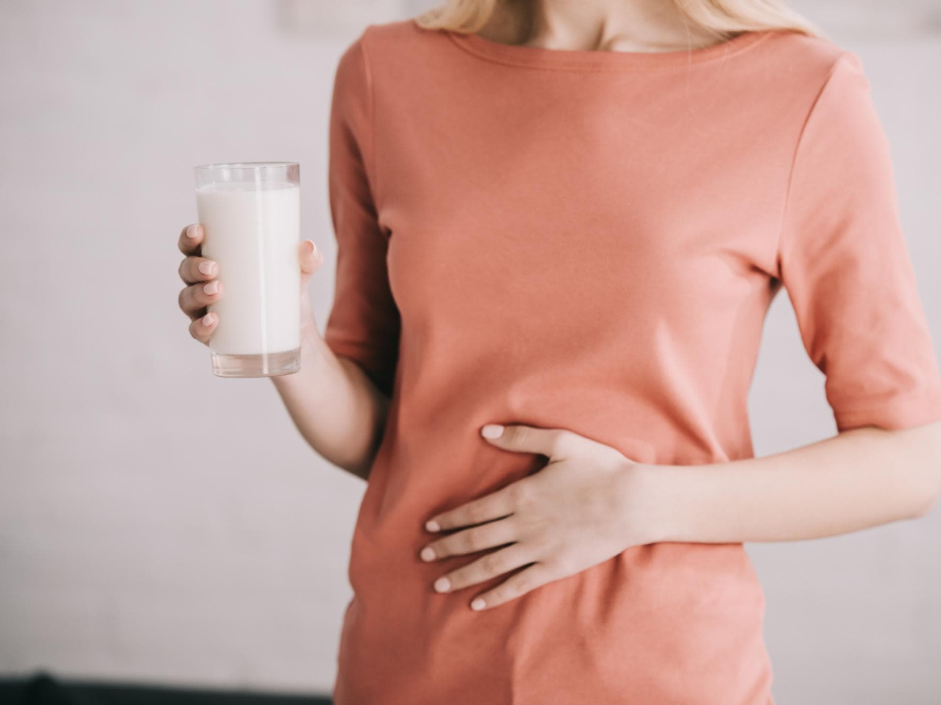 Frau hält ein Glas Milch in der Hand und hat Bauchschmerzen
