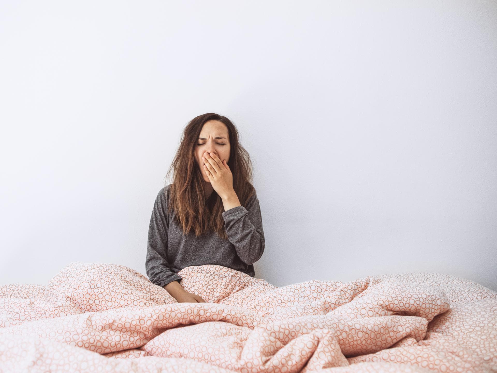 Frau sitzt im Bett und gähnt