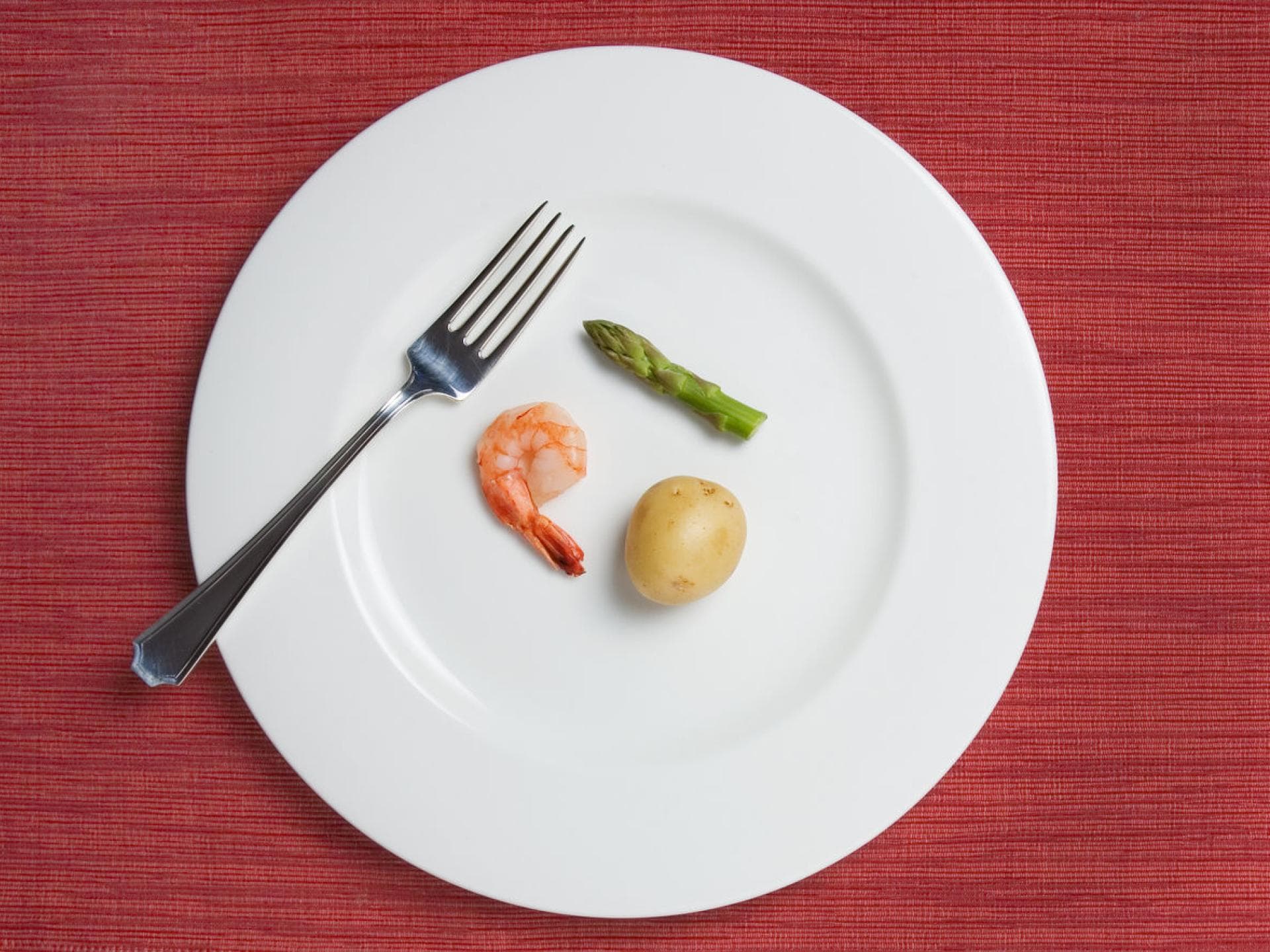 Großer Teller mit einer kleinen Kartoffel, einem Shrimp und einem Stück grünem Spargel darauf