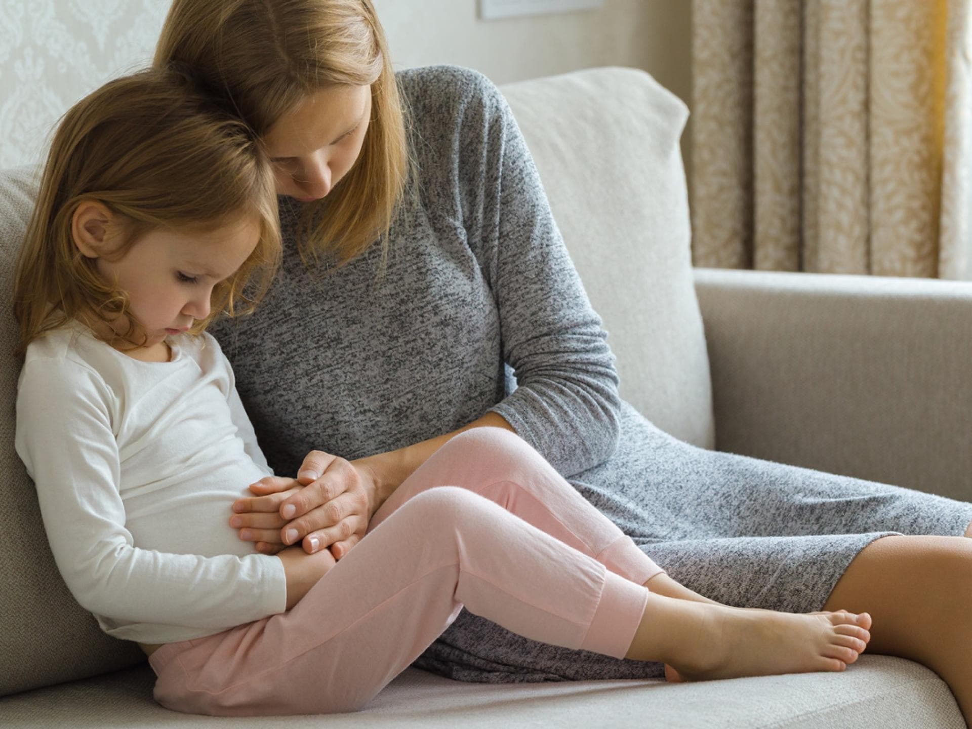 Kind sitzt mit Mutter auf dem Sofa und hält sich den Bauch