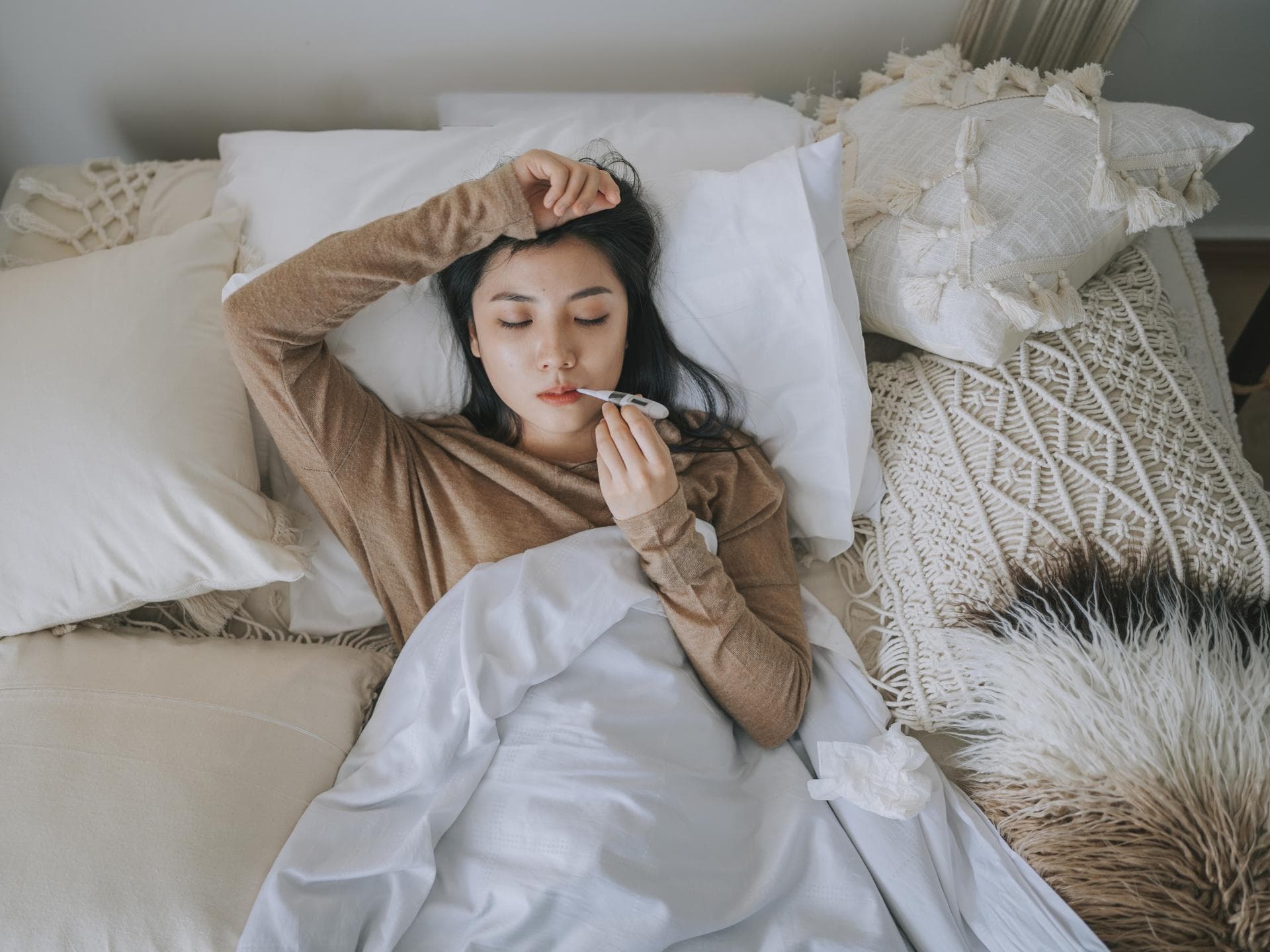 Frau liegt mit Fieberthermometer im Bett