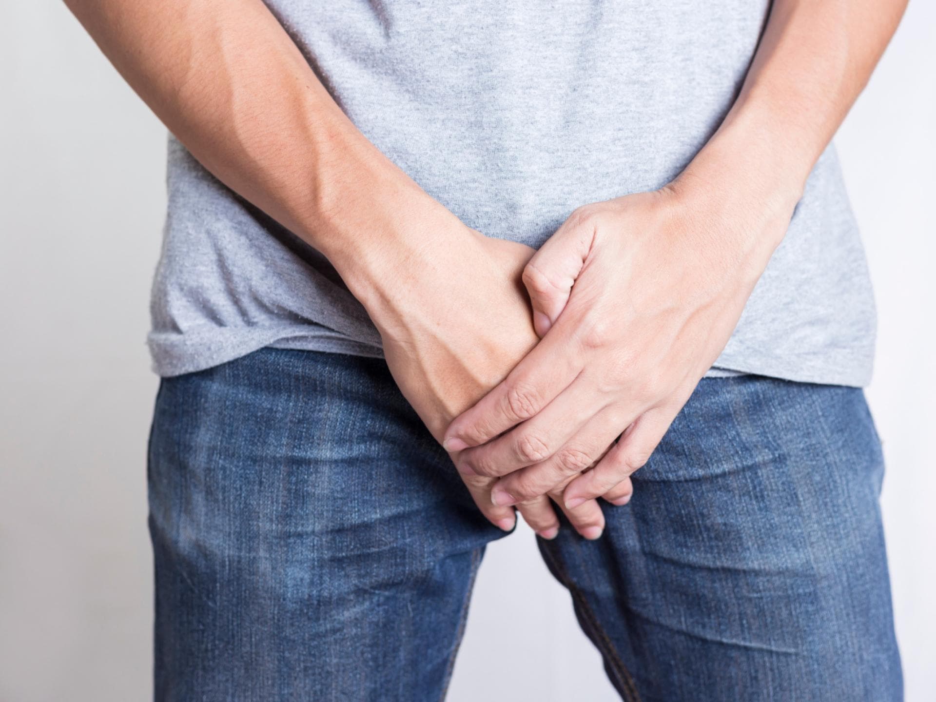 Mann hält sich Hand vor dem Intimbereich