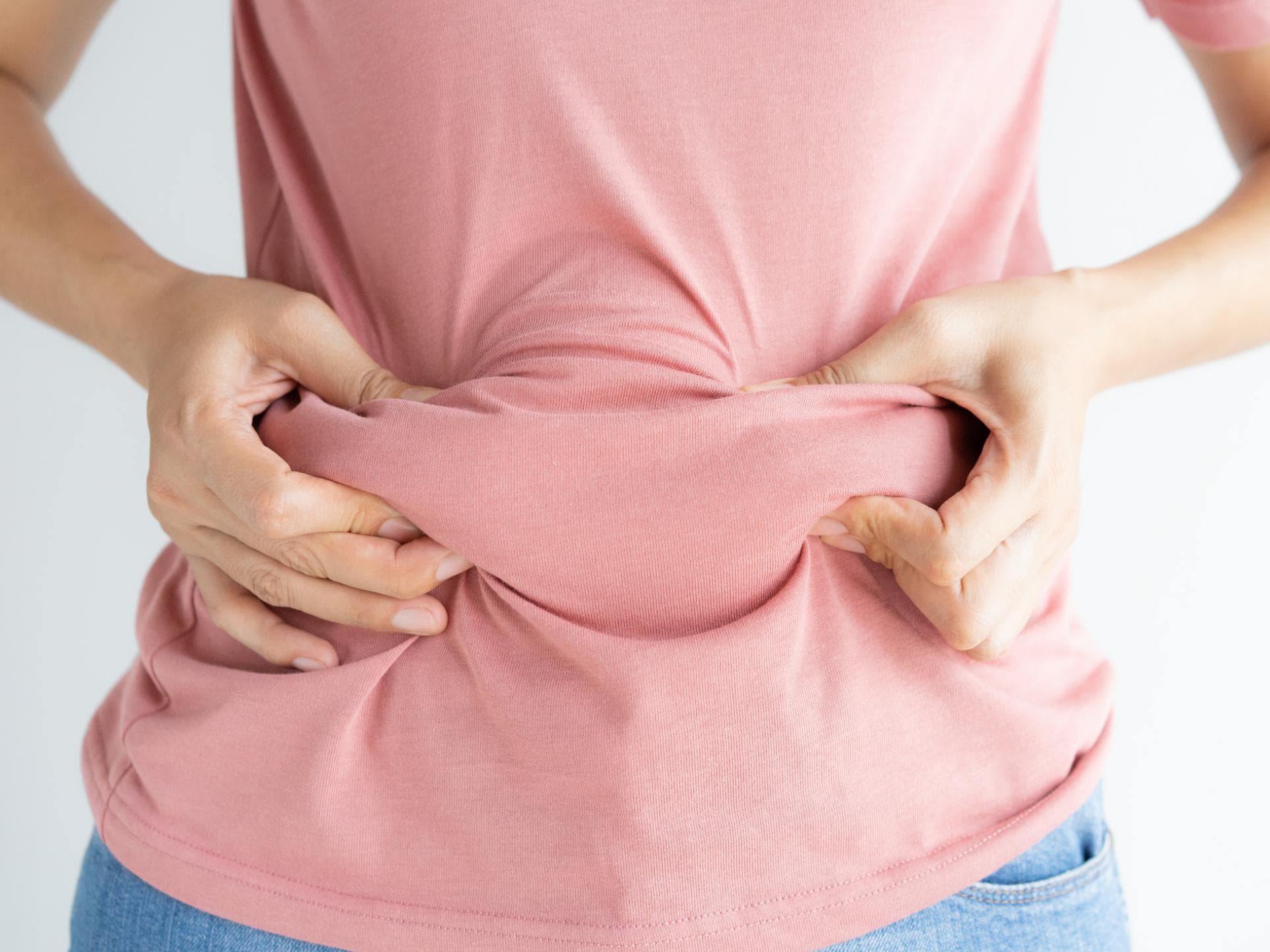 Frau fasst das Fett am Bauch unter ihrem T-Shirt an