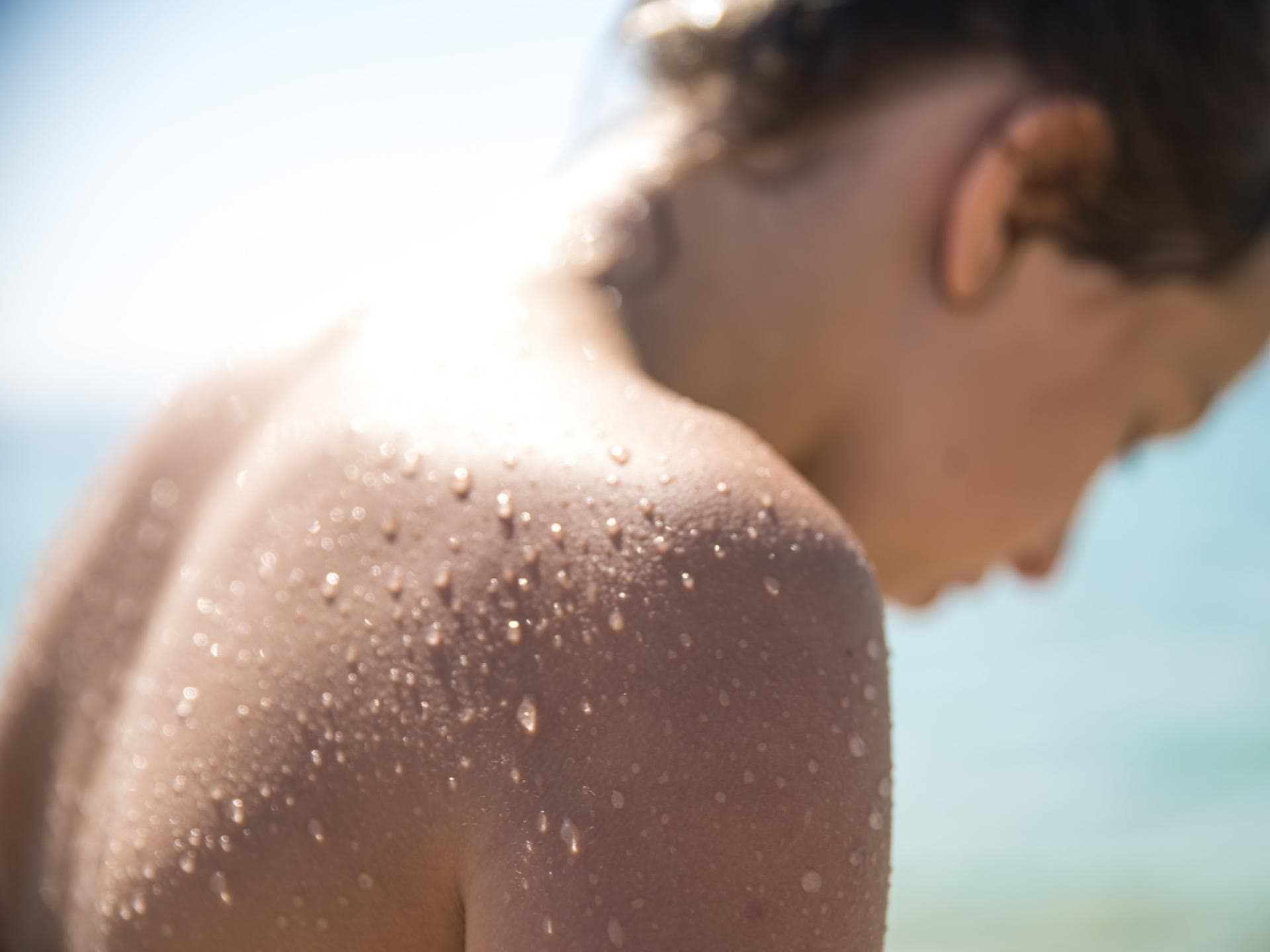 Eine Junge Frau, die sich im Sommer am Wasser befindet und deren Rücken mit Wasserperlen überzogen ist