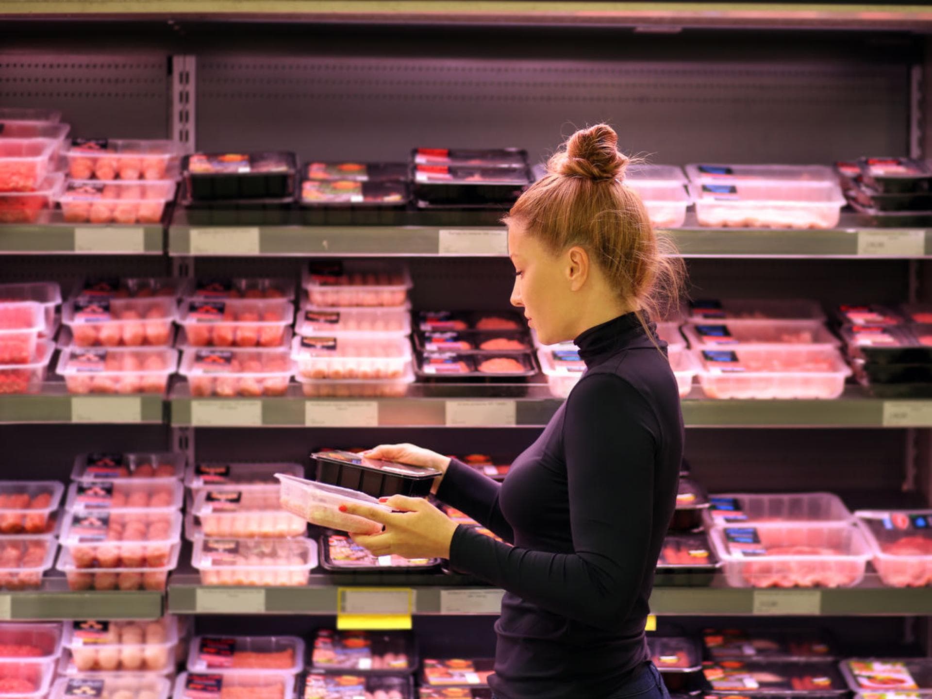 Frau im Supermarkt vor Fleischregal