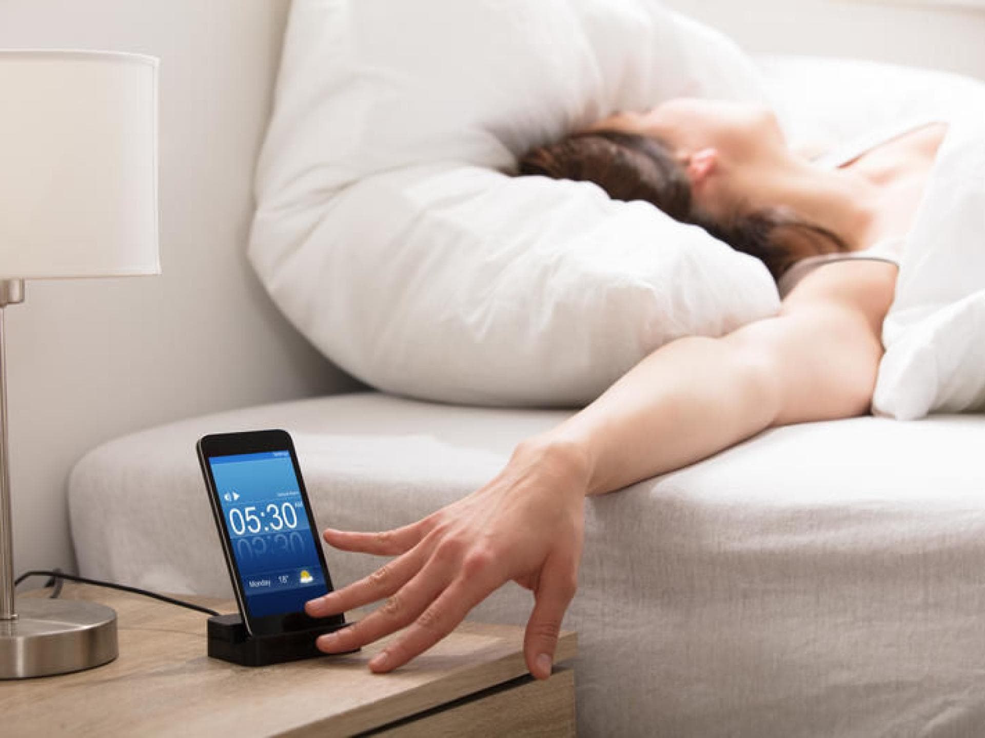 Frau im Bett drückt Snooze Taste Wecker