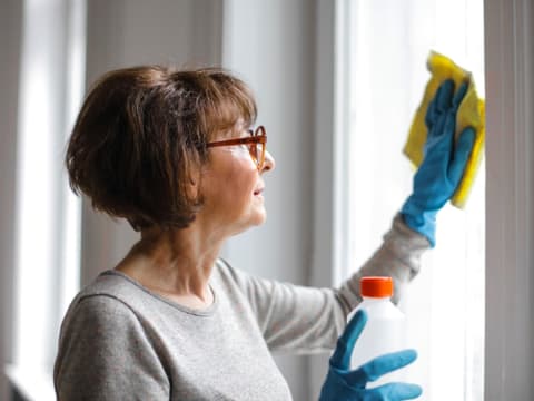 Frau putzt Fenster mit Reinigungsmittel