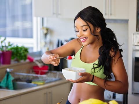 Frau isst Obstsalat in der Küche