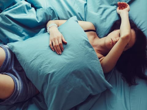 Frau liegt im Bett mit Kopfschmerzen