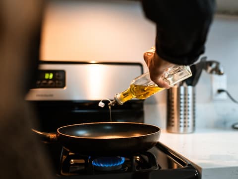 Person gießt Öl in eine Pfanne
