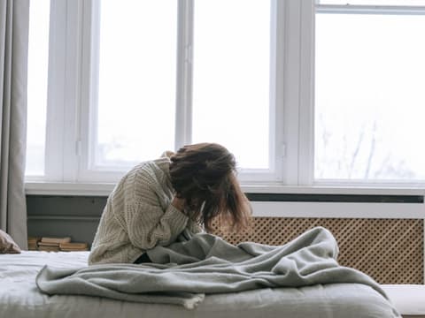 Frau sitzt im Bett und vergräbt ihr Gesicht in ihren Händen