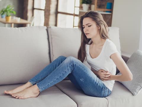Frau sitzt mit Bauchschmerzen auf dem Sofa