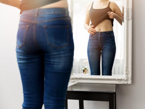Frau betrachtet ihren Bauch im Spiegel