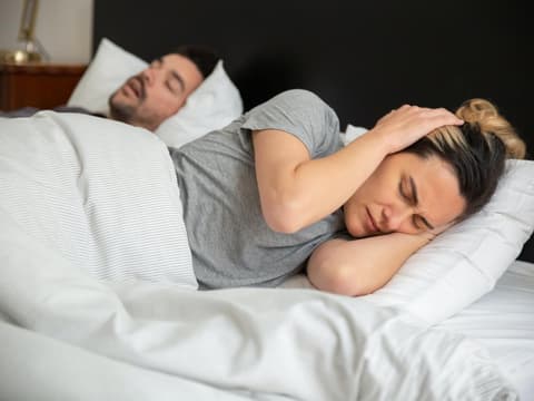Frau hält sich die Ohren zu, weil Mann schnarcht
