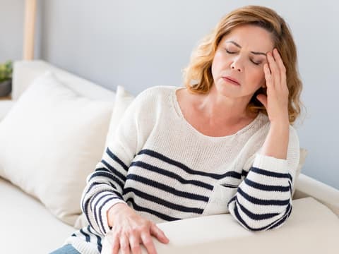 Frau sitzt auf einem Sofa und fasst sich an die Schläfe