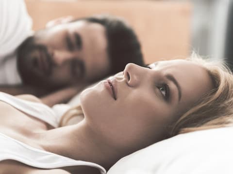 Frau liegt neben schlafendem Partner wach im Bett