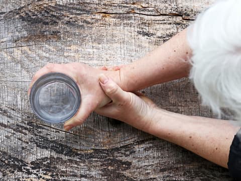 Frau mit grauen Haaren hält Wasserglas in den Händen