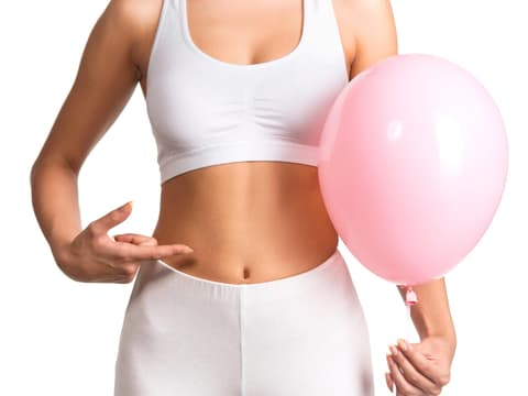Frau mit Luftballon in der Hand zeigt auf ihren Bauch