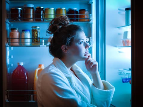 Frau steht Nachts am offenen Kühlschrank