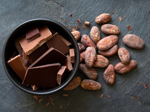 Schokoladenstückchen in einer Keramikschale neben Kakaobohnen 