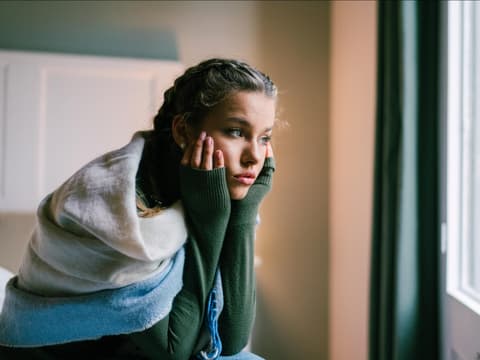 Junge Frau sitzt am Bett und schaut aus dem Fenster