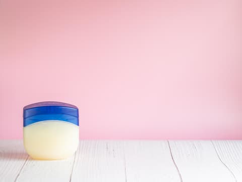 Tigel Vaseline auf Tisch vor pinker Wand