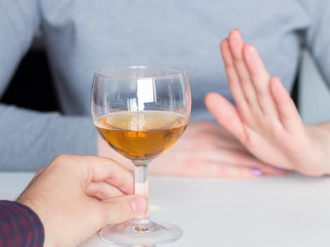 Frau lehnt mit Handgeste ein Glas Wein ab