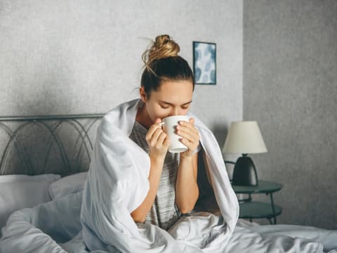 Kranke Frau trinkt Tee im Bett