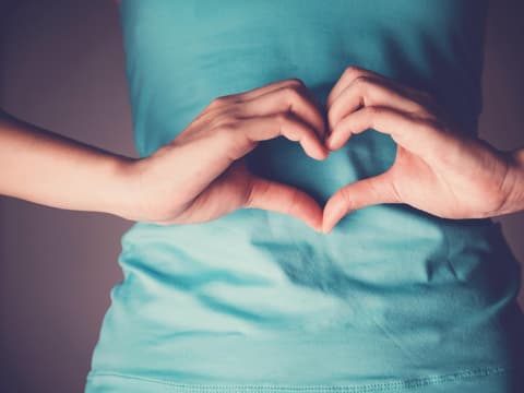 Frau formt Herz mit Händen vor ihrem Bauch