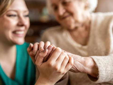 Alte Frau hält Hände mit junger Krankenschwester