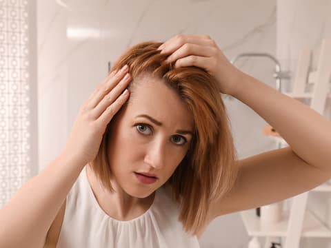 Frau mit Traktionsalopezie betrachtet Haare im Spiegel