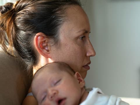Frau mit Wochenbettdepression und Baby auf dem Arm starrt ins Leere