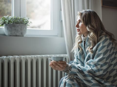 Frau sitzt vor Heizung