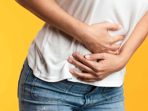 Frau vor gelbem Hintergrund hält sich schmerzenden Bauch