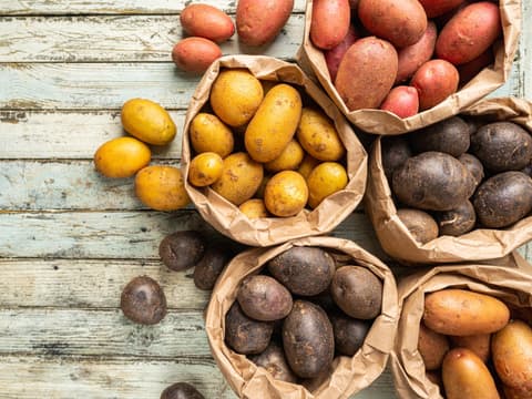 Erntefrische bunte Kartoffeln in Tüten auf Holztisch