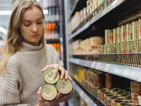 Frau nimmt Konserven aus Supermarktregal