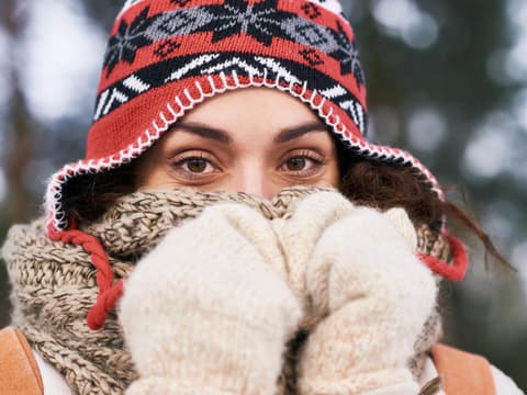 Frau mit Schlappmütze wärmt Nase im Winter unter dickem Schal