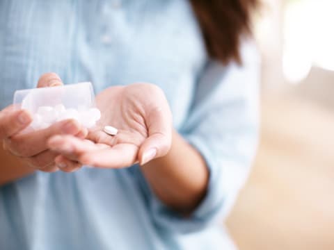 Frau schüttet Schmerztabletten auf Hand